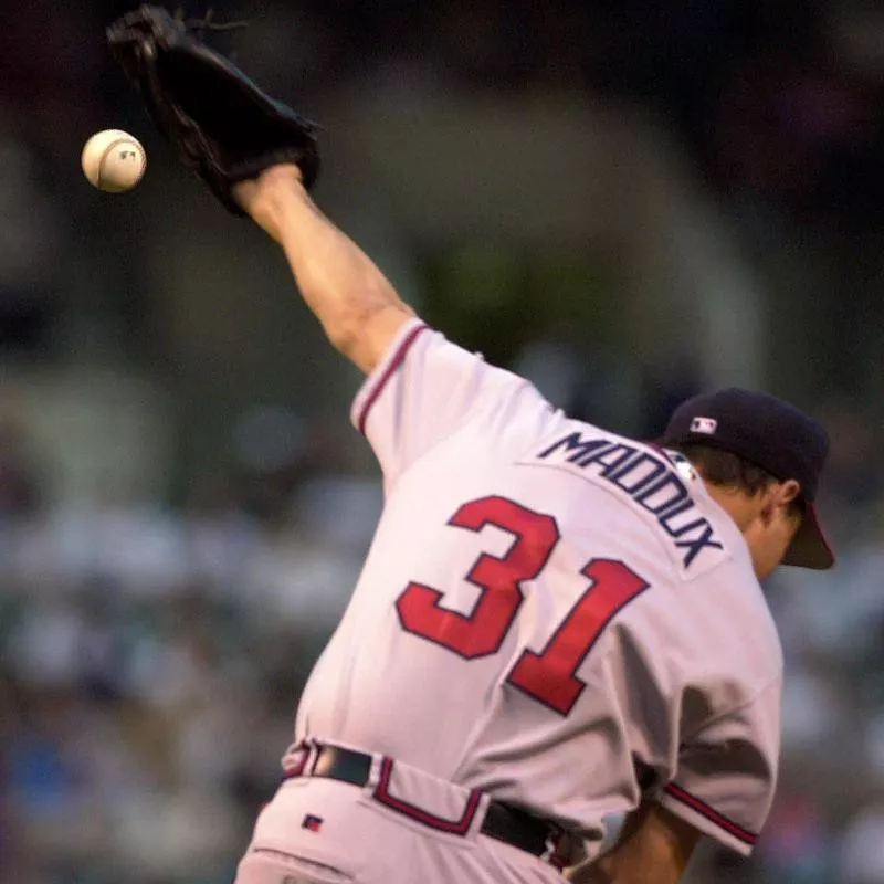 Atlanta Braves pitcher Greg Maddux tries to stop ball hit by Baltimore Orioles Delino DeShields