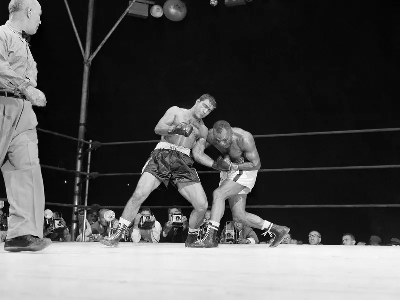 Joe Walcott bends over to cushion effects Rocky Marciano