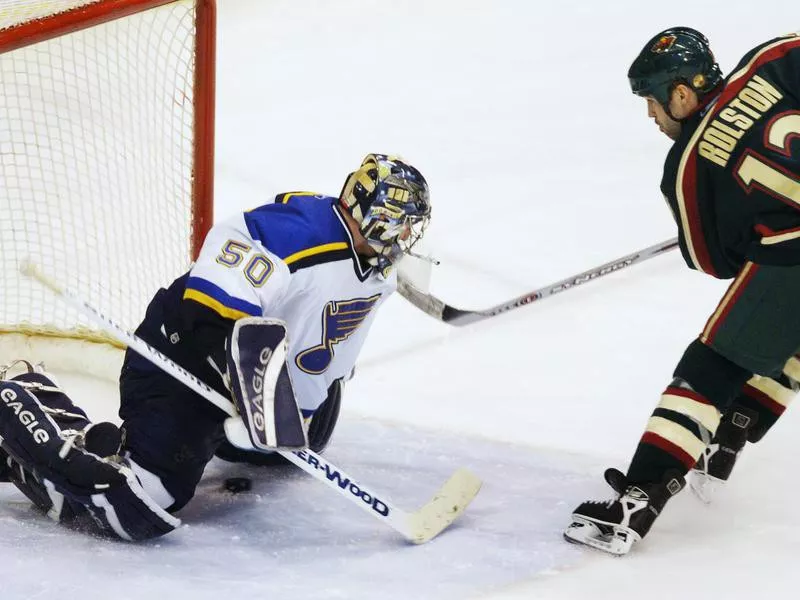 Minnesota Wild's Brian Rolston slides puck under St. Louis Blues goalie Reinhard Divis