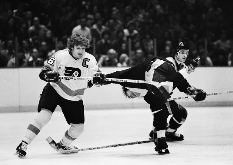 Vancouver Canucks Rick Blight upended by Philadelphia players Bobby Clarke