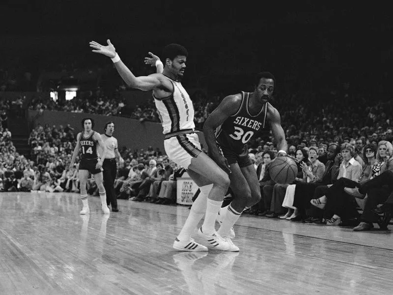 Philadelphia's George McGinnis drives around Trail Blazers' Maurice Lucas