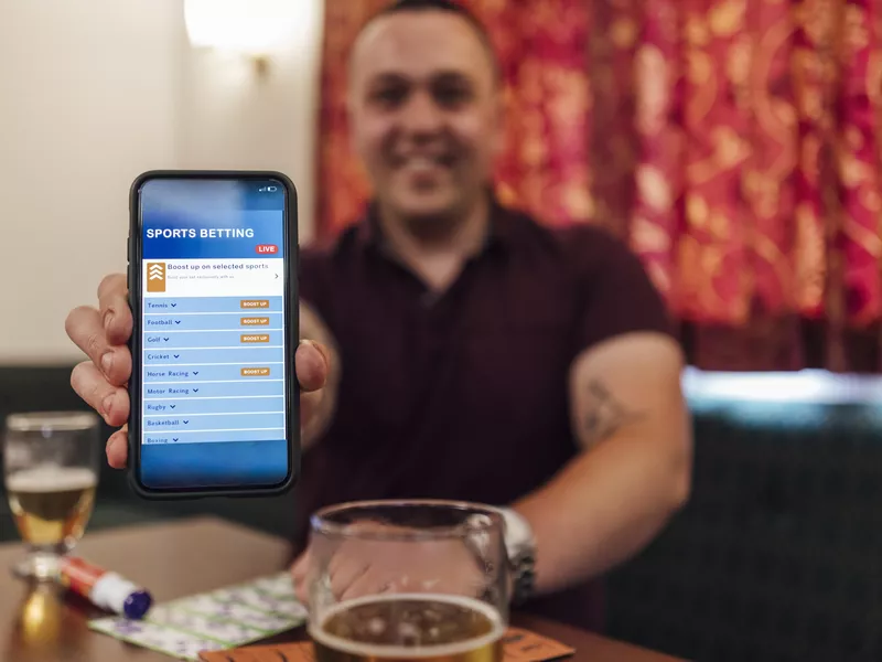 Young man in social club showing a sports betting app on his phone