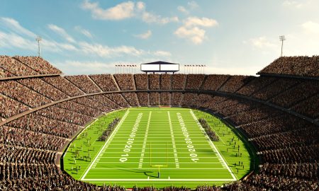 Aerial view on crowded tribune, American football stadium with team on filed. Open air arena with blue sunny sky. Daytime competition. Professional sport, event, tournament, game, championship concept
